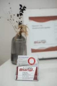 Weiße Empfangstheke bei Autoglas Stangl in Landsberg am Lech mit frischen Blumen und Visitenkarten – freundlicher Eingangsbereich für Kunden bei Steinschlagreparatur, Scheibentausch und Kalibrierung